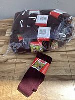 Sixteen pairs of burgundy colored socks, brand Pro Feet, packaged together in clear plastic bag with one pair displayed outside of the bag on wooden surface.
