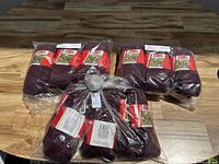 Group of multiple pairs of maroon socks in original packaging, laid out on wooden floor.