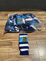 Photo of the full group of approximately 16 pairs of blue and white striped soccer socks in plastic packaging along with one pair laid out in front.