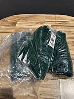 Photo showing multiple pairs of hunter green sports socks in original clear plastic packaging on a wooden surface.