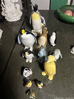 Photo showing 12 various sized penguin figurines with detailed porcelain paint and glaze.