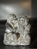 Front view of carved soapstone figurine showing two Inuit figures seated side by side with detailed fur clothing.
