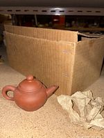 Single small Chinese clay teapot next to a partially opened cardboard box.