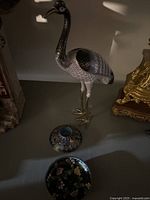 Crane figurine and two cloisonné bowls on a table with shadows, showing detailed enamel work.
