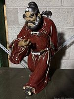 Full view of the ceramic Chinese figurine depicting a bearded man in a red glazed robe, with dynamic posture and facial detail.