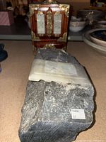 Close-up front view of the large rough stone base topped with a carved white jade piece bearing intricate designs.