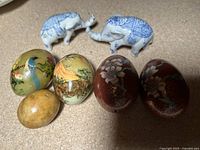 Initial overview of the lot showing 5 decorative eggs and two porcelain elephants on a flat surface