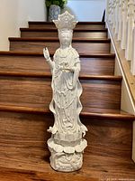 Full view of tall white porcelain Guanyin figurine standing on lotus base on wood stairs