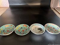 Four small Chinese porcelain dishes lined up on black background showing different decorative styles.
