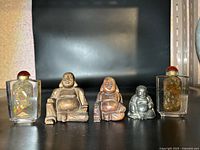 Photo showing three Buddha figurines arranged side by side with two decorative glass snuff boxes at each end on a black surface.