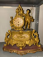 Full view of gilt metal mantel clock with figural decoration and marble base