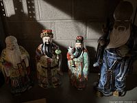 Four Chinese collectible figurines depicting traditional sages or immortals, hand-painted and detailed.