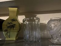 Yellow ceramic vase with black bamboo design, clear glass vase in middle, frosted bird design vase on right