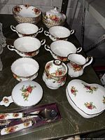Group photo showing multiple pieces of china with floral design and gold rims including bowls, teaspoons, covered sugar bowl, and heart-shaped dish.