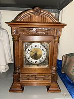 Front view of the large antique wooden mantel clock showing decorative carved pillars, floral motifs, and round clock face with black numerals