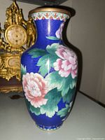 Front and side view of large cloisonne vase displaying pink and white flowers with green leaves on blue background.
