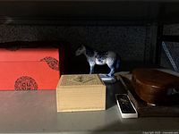 Overview of all items on shelf including red box, beige box, porcelain horse, wooden box, and inkstone
