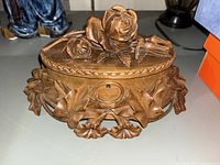 Front view of the oval wood jewelry box with detailed carved roses on lid and sides.