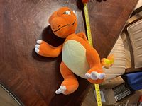 Front side view of Charmeleon stuffed toy lying on a wooden table with a measuring tape showing size.
