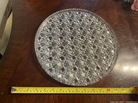Top-down view of the round cut glass serving tray showing starburst pattern and approximate diameter with measuring tape.