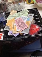 Pokémon Monopoly game money, various colored property cards, important documents, and some tokens on a black plastic game tray.