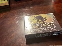Closed box of One Night Ultimate Werewolf board game on a wooden surface.