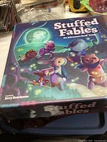 Photo showing the Stuffed Fables game box cover with cartoon stuffed animal characters under a moonlit sky.