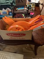 Box containing multiple orange Hot Wheels track pieces, including straight tracks and a circular loop section, displayed on a wooden surface among other household items.