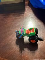 Angle view of a small colorful toy monster trike truck showing side and front details including large rear wheels and handlebar.