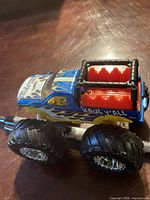 Side view of blue and yellow Haul Y'all monster truck toy with red bed and black roll bar frame on a wooden surface