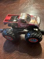 Side view of red monster truck toy showing worn paint and large black wheels with orange rims.