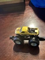 Side view of yellow monster truck toy with flame decals and large black wheels on wooden surface.
