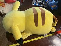 Top view of the large yellow Pikachu stuffed toy showing its size with measuring tape and brown stripes on its back.