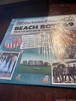 Photo of vinyl record album cover with newspaper style 'The London Telegraph' title and Beach Boys live in London 1969 text, sealed in plastic wrap showing light scratches.