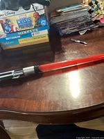 Overall image showing red light saber on wooden table near books and DVDs