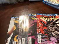 Photo showing six Batman comic books stacked with visible partial front covers featuring characters and titles.