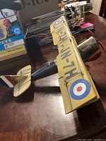 Side view of yellow tin biplane decoration showing wing markings and propeller.