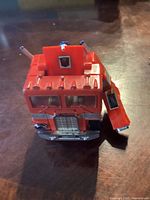 Red cab portion of the vintage Optimus Prime toy showing front grill, windshield with clear windows, two smokestacks, and an open side door on a wooden table.