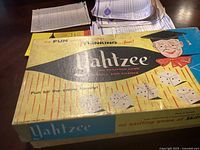 Photo of the Yahtzee game box lid showing vintage design with dice and a cartoon character in graduation attire.