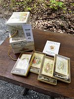 Two sets of Beatrix Potter mini books in decorative boxes with four woven picture cards on a wooden surface.