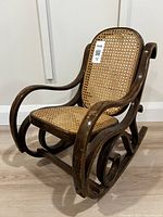 Front angle view of bentwood child rocker showing curved armrests, cane seat and backrest, and wood condition.