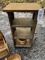 Full view of the wooden caned shelf unit with three shelves standing on gravel ground, showing its measurements and usage wear.
