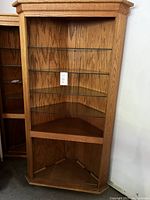 Full view of oak corner cabinet showing 4 glass shelves and open bottom section