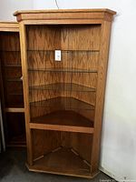 Front view of custom made oak corner cabinet showing three glass shelves, empty interior, and natural oak finish.