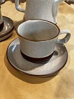 Close up photo of a speckled grey Denby teacup on matching saucer showing brown rim and base trim