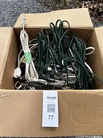 Box full of 12+ assorted extension cords in white and green colors, coiled and tangled inside a cardboard box.