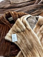 Light beige mink fur stole folded on dark brown fur coat, showing texture and lining