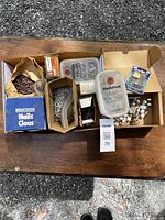 Wide view of all boxes and containers including nails, screws, and miscellaneous hardware items placed on a wooden table outdoors.