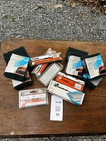 Photo showing multiple packages of Paslode nails and two boxes of 3M heavy-duty stripping scouring pads arranged on wood surface