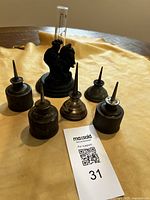 Photo showing six vintage oil tins arranged with a rain gauge in the center on a tan surface.